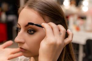 Make-up artist paints eyebrow pencil to beautiful brunette in be photo