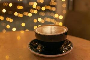 A cup of latte coffee with heart-shaped foam on a table in a cafe, in the background, the lights in a blur are reflected on the table. photo