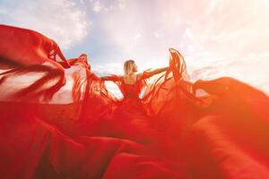 mujer rojo volador vestido. un rubia en un rojo vestir en contra el cielo. posterior ver de un hermosa rubia mujer en un rojo vestir revoloteando en el viento en contra un azul cielo y nubes foto