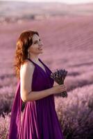 un mujer en un púrpura vestir es en pie en un campo de lavanda flores ella es participación un ramo de flores de flores en su mano. foto