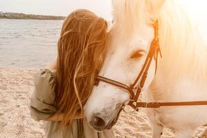 A white horse and a woman in a dress stand on a beach, with the photo