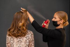 mujer salón peinado. peluquero usos laca para el cabello en clientela pelo en salón, retrato de dos hermosa mujer foto