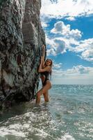 mujer traje de baño mar. atractivo rubia mujer en un negro traje de baño disfrutando el mar aire en el costa alrededor el rocas viaje y vacaciones concepto. foto