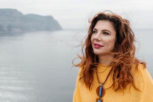 Portrait windswept hair happy woman against a backdrop of mountains and sea. Daylight illuminates the tranquil outdoor setting photo