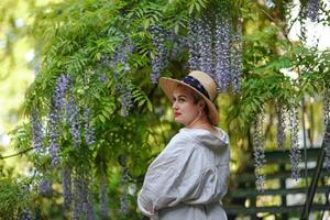 Thoughtful happy mature woman in hat surrounded by chinese wisteria photo