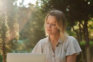 a beautiful mature woman in glasses works on a computer at a white table in nature and spends her day productively photo