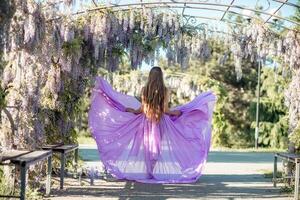 Woman wisteria lilac dress. Thoughtful happy mature woman in purple dress surrounded by chinese wisteria photo