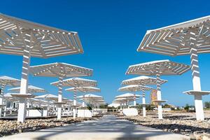 Rows of wooden umbrellas from the sun on the seashore in the morning. Wooden paths on the sand between umbrellas. Beach holiday at the resort. photo