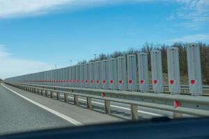 A road with a long line of metal posts with red hearts on them. The road is empty and the sky is clear. photo