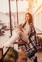 A middle-aged woman in a beige sweater with a blue mug in her hands is in a street cafe on the veranda photo