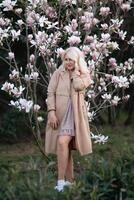 A woman is holding a magnolia flower in her hand and standing in front of a tree. Concept of serenity and beauty, as the woman is surrounded by nature and the flower adds a touch of color. photo