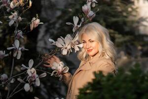 un mujer es en pie en frente de un magnolia árbol con blanco flores ella es participación un flor en su mano y mirando a él. concepto de serenidad y apreciación para naturaleza. foto