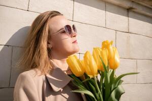 Woman holding yellow tulips, leaning against stone wall. Women's holiday concept, giving flowers. photo