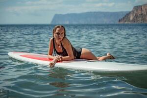 Woman sap sea. Sports girl on a surfboard in the sea on a sunny summer day. In a black bathing suit, he lies on a sap in the sea. Rest on the sea. photo