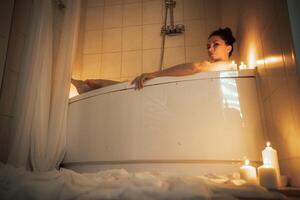 A woman is sitting in a bathtub with candles lit around her. Scene is relaxing and calming. photo