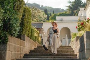 Woman on the stairs in the park. A middle-aged lady in a hat in a white outfit with a bag walks around the Livadia Palace photo