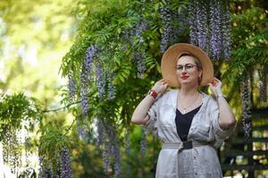 Thoughtful happy mature woman in hat surrounded by chinese wisteria photo