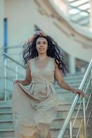 un mujer en un largo vestir es caminando arriba un conjunto de escaleras. ella es vistiendo rojo uña polaco y tiene un sonrisa en su rostro. foto