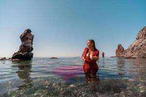 A woman in a red dress is sitting in the water. The water is clear and the sky is blue. photo