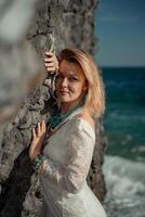 Middle aged woman looks good with blond hair, boho style in white long dress on the beach decorations on her neck and arms. photo