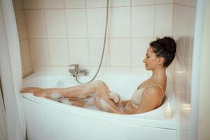 un mujer es sentado en un bañera con burbujas y velas ella es sonriente y ella es disfrutando su baño. foto