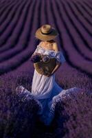 un mujer es en pie en un campo de púrpura lavanda flores, vistiendo un Paja sombrero y participación un cesta de flores foto