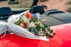 A bouquet of flowers is sitting on the hood of a red car. The flowers are white and red, and they are arranged in a vase. Concept of romance and love. photo