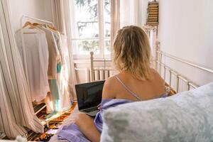 A top view of a woman in a purple nightgown using a laptop on a bed, suggesting that she is working or studying from the comfort of her own home. photo