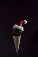 A cone shaped ice cream cone with a red hat on top. The cone is made of pine cones and the hat is made of white and red fabric. photo