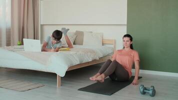 casa isolamento, distância aprendizado, controlo remoto trabalhar, ginástica às lar, conectados treinamento, família quarentena. mulher fazendo abdômen exercício enquanto deitado em a chão. Garoto durante conectados Aprendendo video