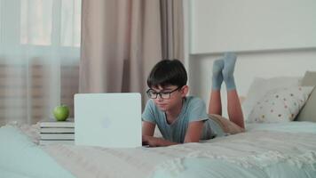 Home Isolation, Online Learning, Remote Work, New Education. Boy doing homework using online technologies while lying on the bed at home video