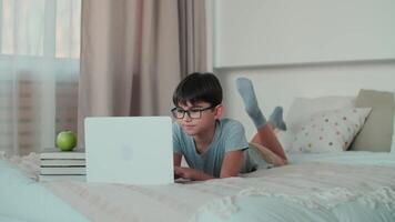 Home Isolation, Online Learning, Remote Work, New Education. Schoolboy doing homework using online technologies while lying on the bed at home video