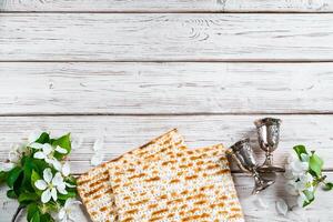 Happy Passover flatlay. Jewish matzo bread and wine glasses on white wooden background. photo