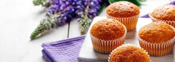 Delicious muffins and purple lupine flowers on white wooden background. photo