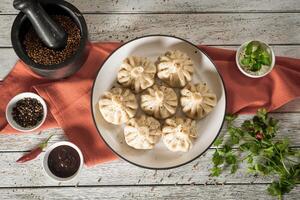 Close up to Caucasian khinkali dumplings dish served on plate. Background with ingredients and scattered spices photo