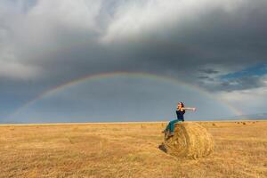 hermosa joven niña en un campo con Paja en un antecedentes de arco iris foto