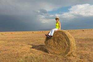 hermosa joven niña en un campo con Paja en un antecedentes de arco iris foto