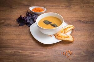 Red lentil soup with spices, herbs, bread in a rustic metal saucepan and bowls, wood backdrop, top view. photo