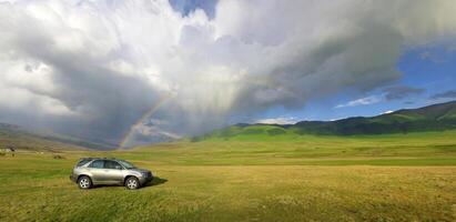 fuera del camino coche muy en montañas en contra un hermosa arco iris foto