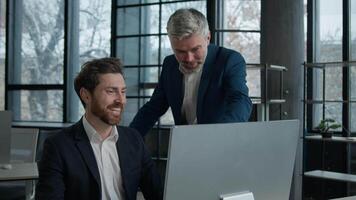 Two successful excited Caucasian businessmen workers looking computer screen in office men business partners investors coworkers celebrating successful giving high five rejoice achieving good result video