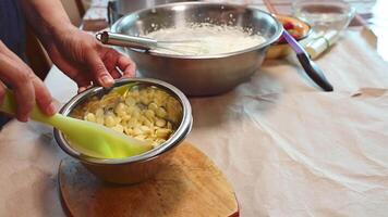 Close-up pastry chef melting white Belgian confectionery chocolate callets in metal bowl, preparing icing to decorate the top of cakes or add to whipped cream while making sweet dessert. Confectionery video