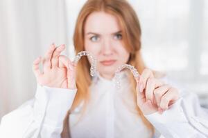 dental cuidado.sonriendo niña con tirantes en su dientes sostiene alineadores en su manos y muestra el diferencia Entre ellos foto