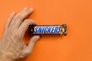 Hand holding a Snickers chocolate bar. Snickers bars are produced by Mars Incorporated. Snickers was created by Franklin Clarence Mars in 1930 photo