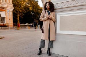 Outdoor fashion portrait of glamour sensual young stylish black  lady wearing trendy fall outfit  , grey velvet  sweater and beige wool coat. Cold season.Warm clothes. Full length. photo