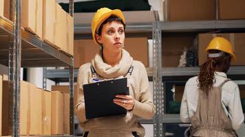 Depot manager counting number of products in stockroom, checking packages with merchandise on industrial racks. Employee using papers to look at inventory list. Handheld shot. photo