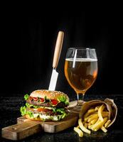 hamburguesa con un cuchillo, papas fritas, cerveza en un vaso. foto