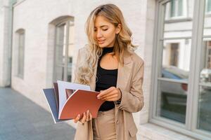 Sucsessful blond business woman posing in stylish suit outdoor. Holding  bdesigner catalogs. photo