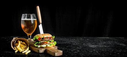 hamburguesa con un cuchillo, papas fritas, cerveza en un vaso. foto