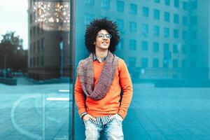 Young curly black African American with glasses walks through the city streets against a skyscraper photo