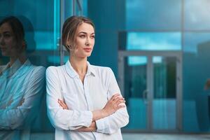 mujer de negocios exitoso mujer negocio persona en pie brazos cruzado al aire libre corporativo edificio exterior. pensativo caucásico confianza profesional negocio mujer medio años foto